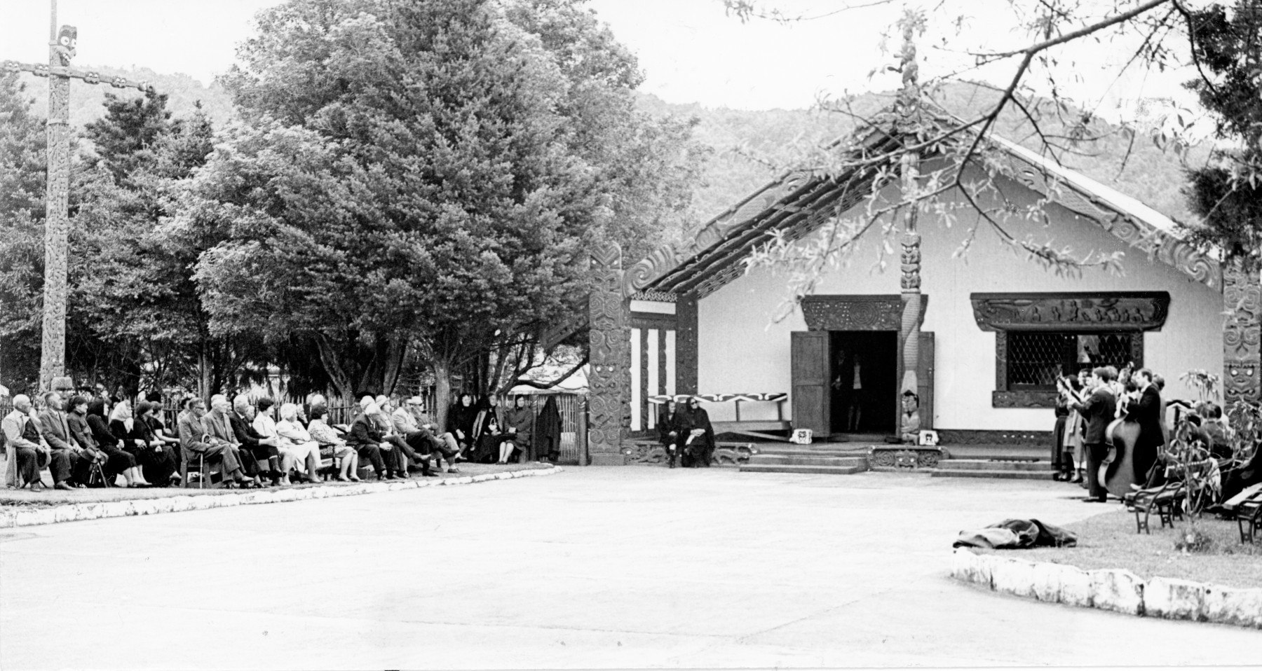 Maori Queen surrounded by her elders and councillors listen to a song from 25 of the cast of Anything to Declare. The venue is the Turangawaewae Marae, or royal courtyard, at Ngaruawahia, in 1970.